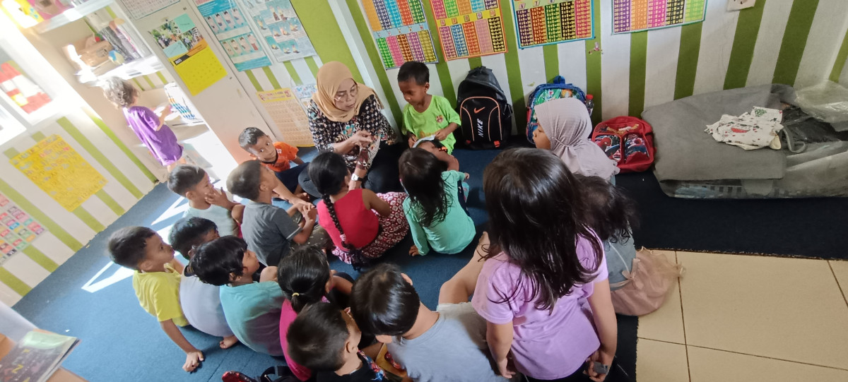 Anak-anak kelas rumah singgah sedang belajar dan mendengarkan cerita bu guru dari pengelola
