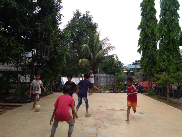Anak - anak bermain sepak bola di lapangan mini basket
