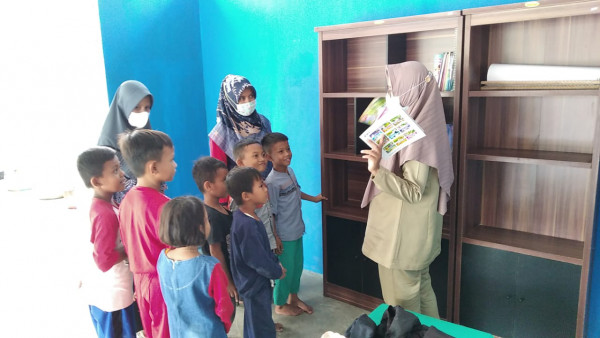 Penyuluh KB bersama pengurus perpustakaan mengajak anak-anak yang bermain di balai dusun untuk membaca buku