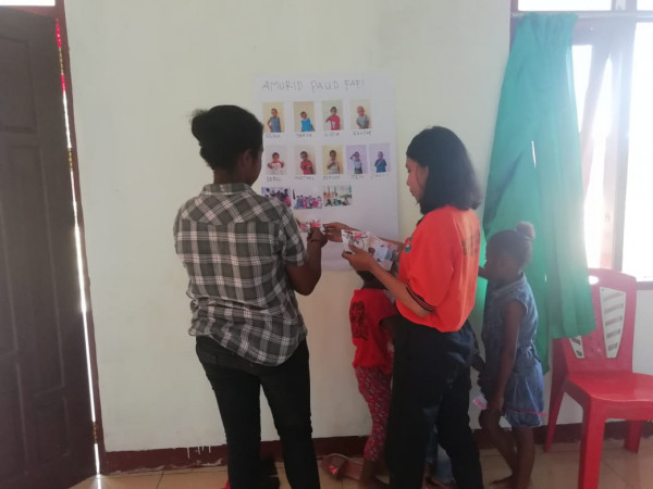 ibu guru bersama mahasiswa Nani Bili membantu menempelkan hasil dari anak PAUD